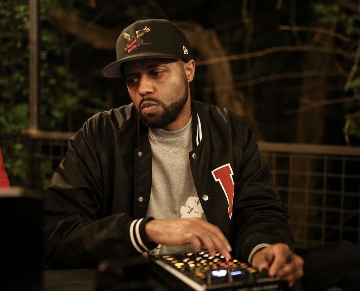 Easy Listening Section in a black varsity jacket and fitted cap, playing pads on a Maschine outdoors at night.